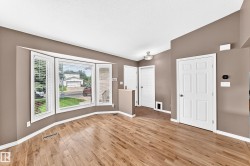 Spacious interior featuring wood-finish flooring, a prominent bay window with white blinds, and neutral-toned walls - 