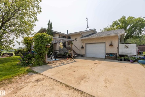 Stucco exterior featuring an attached garage with a white overhead door, an exterior staircase, and a pergola-covered patio - 59228 Rg Rd 11, Rural Westlock County, AB 
