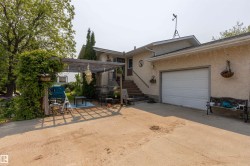 Exterior featuring an attached garage with a white panel door, stucco siding, and a covered pergola with lush foliage - 