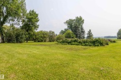 Expansive green lawn surrounded by mature trees and shrubs, with distant fields visible - 