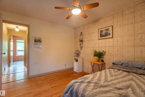 Room featuring wood-finish flooring, a decorative accent wall, a ceiling fan with integrated lighting, and a doorway leading to an interior corridor with a window - 59228 Rg Rd 11, Rural Westlock County, AB 