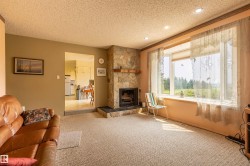 Living area featuring a stone-clad fireplace with a wood mantel, a large bay window, recessed ceiling lighting, and textured carpeting - 