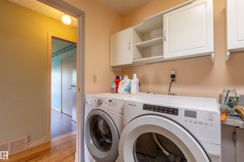 Dedicated laundry area featuring a front-load washing machine, top-load washing machine, and upper white cabinetry - 59228 Rg Rd 11, Rural Westlock County, AB 