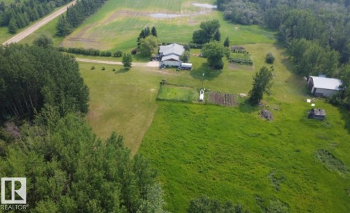 Expansive property featuring a main residence with a light-colored roof, multiple outbuildings, and cultivated garden plots - 59228 Rg Rd 11, Rural Westlock County, AB 