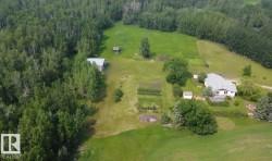 Spacious property featuring a single-story residence with a light-colored roof, multiple outbuildings, cultivated garden plots, and expansive green lawns bordered by mature trees - 