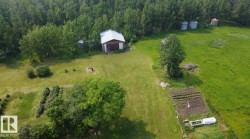Expansive green space featuring a large barn with a metal roof, multiple garden plots, mature trees, and additional storage silos - 