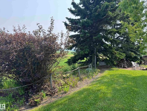 Lush green lawn with mature evergreen trees, dense shrubbery, and a rustic rope fence - 59228 Rg Rd 11, Rural Westlock County, AB 
