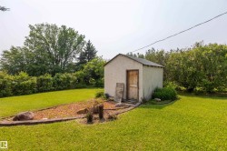 Exterior storage shed with a wood door, surrounded by a manicured lawn and mature trees - 