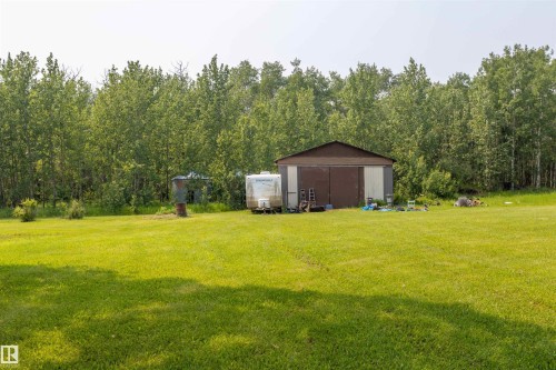 Expansive green lawn extending towards a brown and gray utility building with a pitched roof, backed by a dense treeline - 59228 Rg Rd 11, Rural Westlock County, AB 