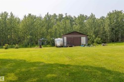 Expansive green lawn extending towards a brown and gray utility building with a pitched roof, backed by a dense treeline - 