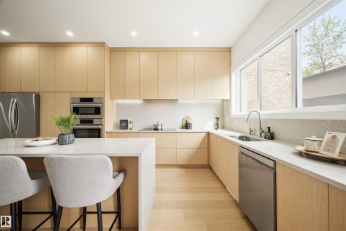 Modern kitchen featuring light wood-finish cabinetry, light stone countertops, stainless steel appliances, and a built-in oven stack - 14037 104 Avenue, Edmonton, AB - Indoor Photo Showing Kitchen With Upgraded Kitchen