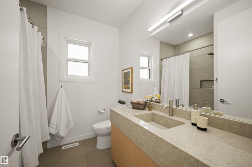 Modern bathroom featuring a built-in vanity with an integrated sink, a large wall-mounted mirror, two windows, and a tiled shower with a recessed niche - 14037 104 Avenue, Edmonton, AB - Indoor Photo Showing Bathroom