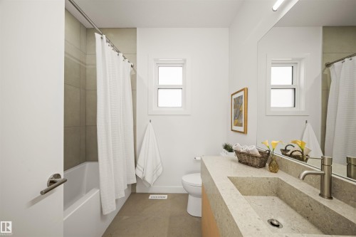 Bathroom featuring a stone-finish integrated sink, brushed nickel faucet, full-width mirror, and a white bathtub with subway tile surround - 14037 104 Avenue, Edmonton, AB - Indoor Photo Showing Bathroom