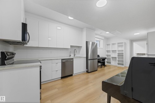 Modern kitchen area featuring white flat-panel cabinetry, stainless steel appliances, a white subway tile backsplash, light-toned wood-finish flooring, and recessed lighting - 14037 104 Avenue, Edmonton, AB - Indoor Photo Showing Kitchen