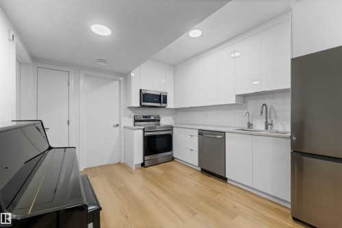 Modern kitchen featuring white flat-panel cabinetry, stainless steel appliances, a subway tile backsplash, and light wood-finish flooring - 14037 104 Avenue, Edmonton, AB - Indoor Photo Showing Kitchen
