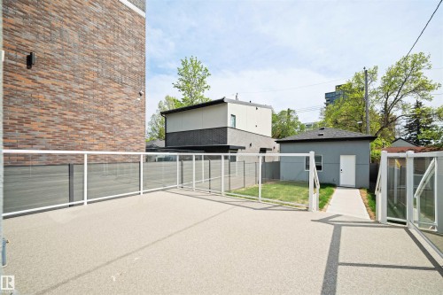 Expansive outdoor patio featuring a glass railing system, a dedicated side yard area with a concrete pathway, a detached structure with a white door, and a brick exterior wall - 14037 104 Avenue, Edmonton, AB - Outdoor With Exterior
