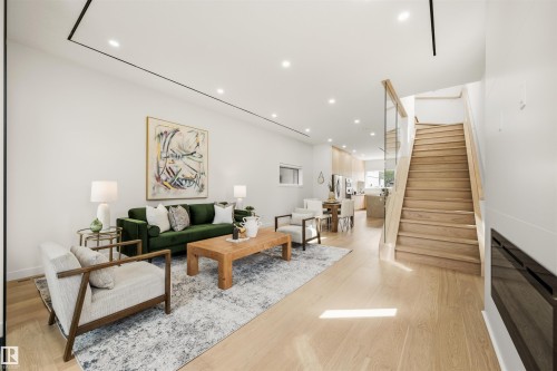Open-concept living area with light wood-finish flooring, recessed lighting, a built-in fireplace, and a light wood staircase featuring glass panel railings - 14037 104 Avenue, Edmonton, AB - Indoor