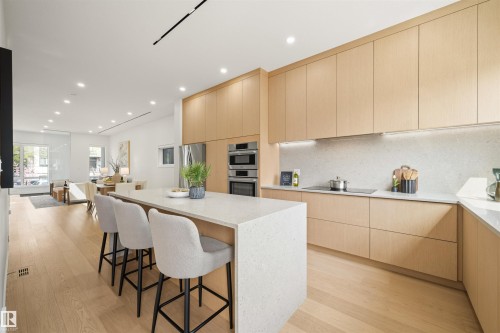 Modern kitchen featuring light wood-finish cabinetry, integrated stainless steel appliances, and a substantial island with a light-toned countertop - 14037 104 Avenue, Edmonton, AB - Indoor Photo Showing Kitchen With Upgraded Kitchen