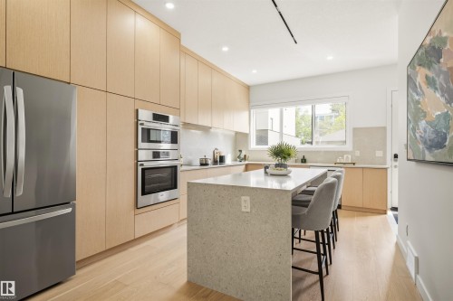 Modern kitchen featuring light wood-finish cabinetry, stainless steel appliances, a built-in oven and microwave, a large center island with a light-toned countertop, and recessed lighting - 14037 104 Avenue, Edmonton, AB - Indoor Photo Showing Kitchen With Upgraded Kitchen