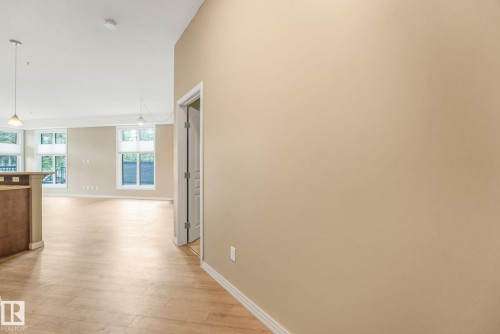 Open-concept interior featuring wood-finish flooring, neutral wall tones, white trim, and multiple large windows - 126 10531 117 Street, Edmonton, AB 