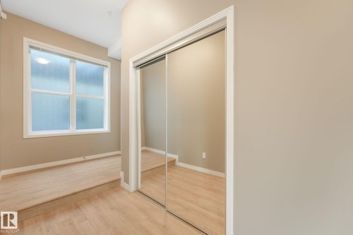 Mirrored closet doors providing visual depth, accompanied by wood-finish flooring and a multi-pane window - 126 10531 117 Street, Edmonton, AB 