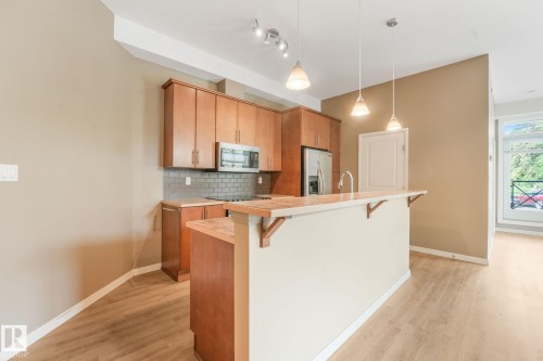 Kitchen featuring wood cabinetry, stainless steel appliances, a subway tile backsplash, and a breakfast bar with pendant lighting - 126 10531 117 Street, Edmonton, AB 