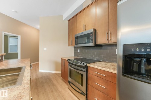Kitchen featuring wood-finish flooring, light wood cabinetry, stainless steel appliances, and a gray subway tile backsplash - 126 10531 117 Street, Edmonton, AB 