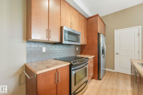 Kitchen featuring wood cabinetry, stainless steel appliances, subway tile backsplash, and light-toned countertops - 126 10531 117 Street, Edmonton, AB 