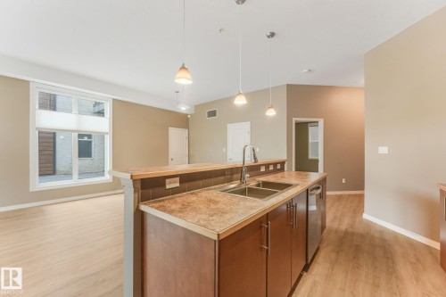 Kitchen island featuring a double basin stainless steel sink, a stainless steel dishwasher, pendant lighting, and wood-finish flooring - 126 10531 117 Street, Edmonton, AB 