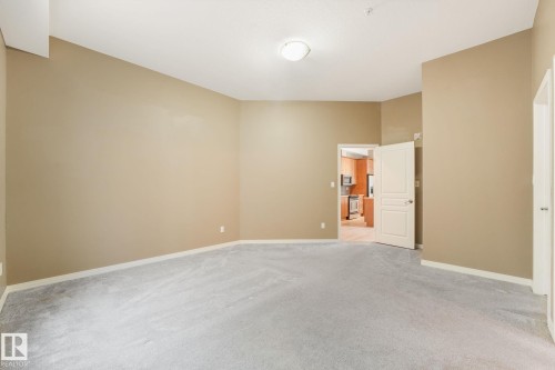 Spacious room featuring neutral-toned walls, light-colored carpeting, white trim, and an overhead flush-mount light fixture - 126 10531 117 Street, Edmonton, AB 