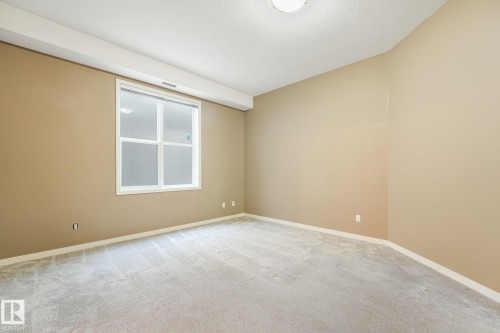 Bedroom featuring neutral carpeting and walls, a window with white trim, and a ceiling-mounted light fixture - 126 10531 117 Street, Edmonton, AB 