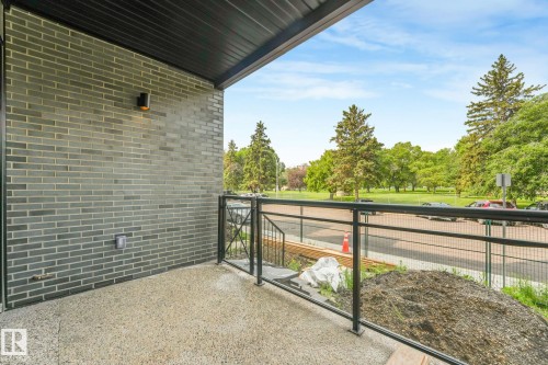 Private balcony featuring a dark brick exterior, exposed aggregate flooring, and a black metal railing - 126 10531 117 Street, Edmonton, AB 