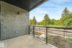 Private balcony featuring a dark brick exterior, exposed aggregate flooring, and a black metal railing - 