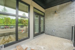 Private balcony featuring a textured concrete surface, dark brick exterior wall, and black metal railing - 