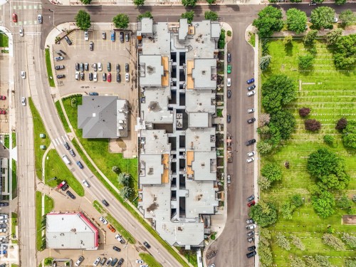 Aerial perspective showcasing a multi-unit residential building with flat rooflines, a dedicated parking lot, and bordering a lush green space - 126 10531 117 Street, Edmonton, AB 