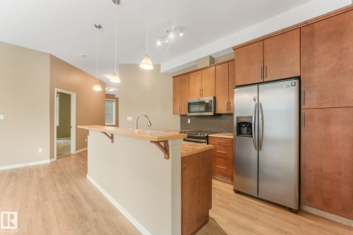 Kitchen featuring wood-finish flooring, stainless steel appliances, pendant lighting, track lighting, and a breakfast bar with a sink and faucet - 126 10531 117 Street, Edmonton, AB 