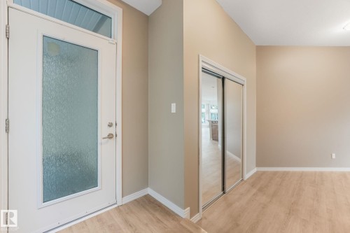 Entryway featuring a white door with frosted glass and transom window, mirrored closet doors, wood-finish flooring, and neutral wall tones - 126 10531 117 Street, Edmonton, AB 