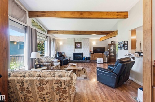 Living area featuring wood-finish flooring, exposed ceiling beams, a white brick fireplace, and large picture windows - 13121 122 Street, Edmonton, AB 