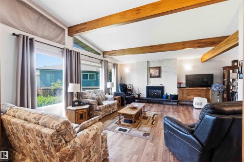 Spacious living area featuring exposed wood beams, wood-finish flooring, and a white brick fireplace with a black hearth - 13121 122 Street, Edmonton, AB 