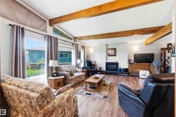 Spacious living area featuring exposed wood beams, wood-finish flooring, and a white brick fireplace with a black hearth - 