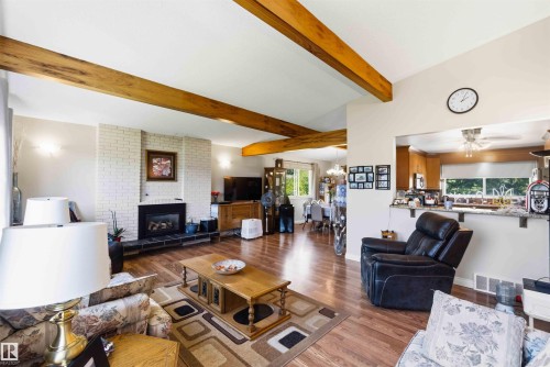 Spacious living area featuring wood-finish flooring, exposed ceiling beams, and a white brick fireplace with a black hearth - 13121 122 Street, Edmonton, AB 
