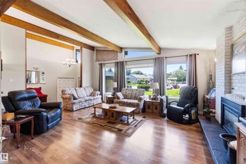 Spacious living area featuring wood-finish flooring, exposed ceiling beams, and a brick-faced fireplace with a dark-toned hearth - 13121 122 Street, Edmonton, AB 