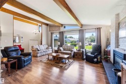 Spacious living area featuring wood-finish flooring, exposed ceiling beams, and a brick-faced fireplace with a dark-toned hearth - 