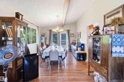Spacious dining area featuring wood-finish flooring, a vaulted ceiling with exposed beam, and ample natural light from multiple windows and a glass-paneled door leading to an exterior balcony - 