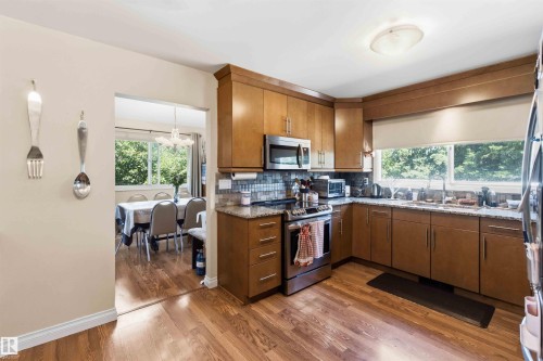 Kitchen featuring wood-finish flooring, wood cabinetry with brushed nickel hardware, stainless steel appliances, and stone countertops - 13121 122 Street, Edmonton, AB 