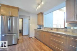 Kitchen featuring wood-finish flooring, light wood cabinetry, stone countertops, a tile backsplash, and a stainless steel refrigerator - 