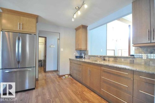 Kitchen featuring wood-finish flooring, light wood cabinetry, stone countertops, a tile backsplash, and a stainless steel refrigerator - 13121 122 Street, Edmonton, AB 