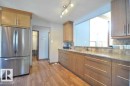 Kitchen featuring wood-finish flooring, light wood cabinetry, stone countertops, a tile backsplash, and a stainless steel refrigerator - 13121 122 Street, Edmonton, AB 