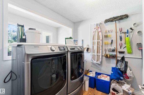 Dedicated laundry area featuring a window, wood-finish flooring, a white pegboard organizational wall, and a built-in shelf above the laundry units - 13121 122 Street, Edmonton, AB 