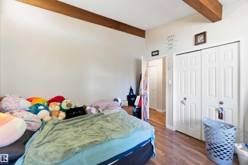 Room featuring wood-finish flooring, two exposed wood beams, and a white bi-fold closet door - 13121 122 Street, Edmonton, AB 